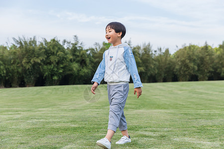 挎包走路的男孩可爱儿童在草地游玩背景