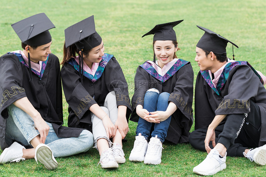 穿学士服的毕业生坐在草坪山聊天图片