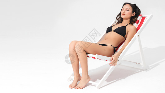 黑色比基尼泳装美女坐在沙滩躺椅上背景图片