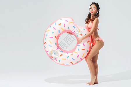 粉色游泳圈穿粉色比基尼的可爱女生拿着甜甜圈泳圈背景