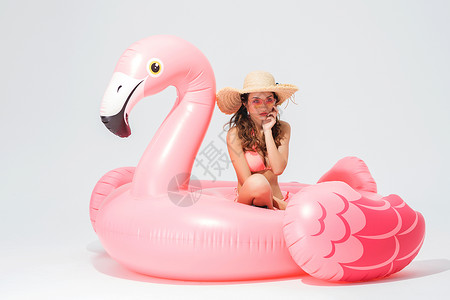 穿粉色比基尼的可爱卖女坐在火烈鸟游泳圈图片