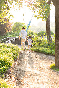 父亲教孩子走路公园里牵手散步父子背影背景