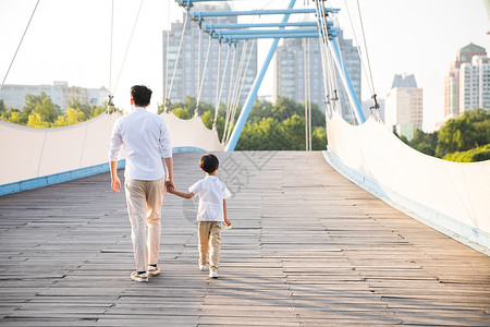 父亲教孩子走路公园里牵手散步父子背影背景