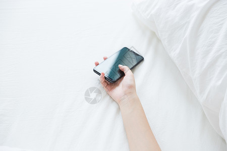 床上女性手拿手机特写背景图片
