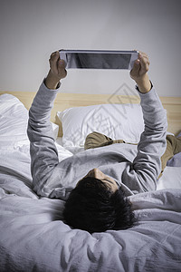 网络交互躺在床上玩平板的男子背景