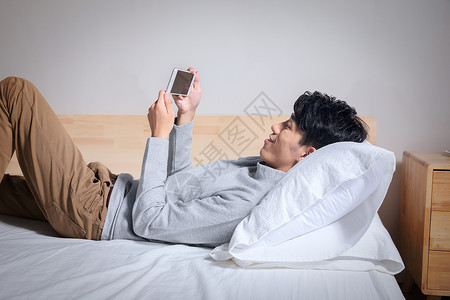 躺在枕头上玩手机的男人图片