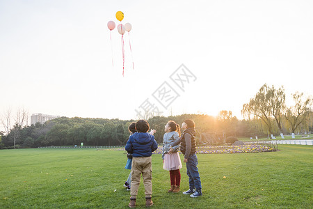 夕阳下儿童们共同放气球背景图片