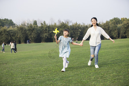 女儿和妈妈拿着风车在草坪上奔跑高清图片