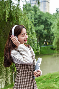 公园带耳机看书的女学生背景图片