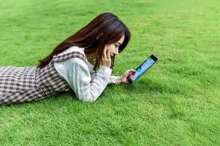 草坪上玩平板的女生图片