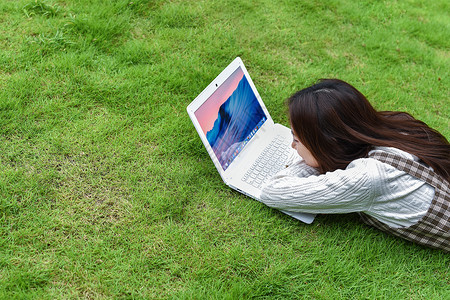 草坪上趴着玩电脑的女生背景图片