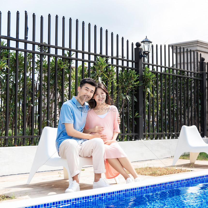 孕妇和丈夫在户外泳池旁坐着休息图片