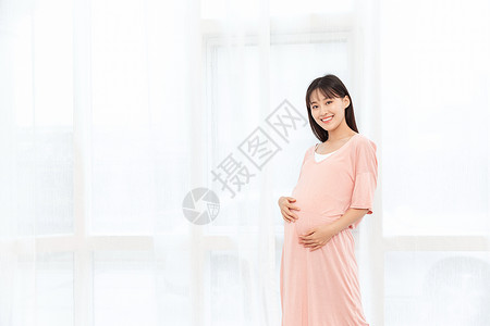 一个孕妇在客厅站着抚摸肚子高清图片
