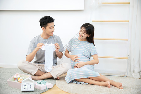 丈夫给孕妇展示自己给孩子买的婴儿衣服图片