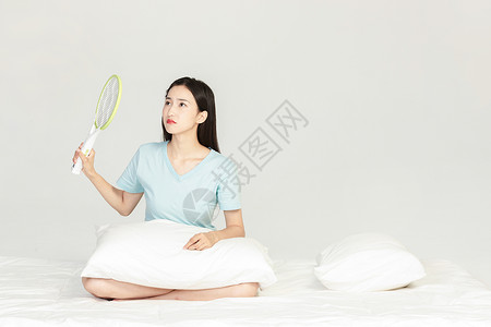 女性坐在床上用电蚊拍背景图片
