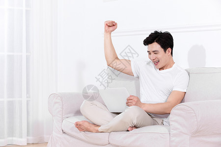 男性坐在沙发上玩电脑感到兴奋高清图片