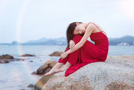 坐在深圳较场尾海边礁石上的红衣少女背景