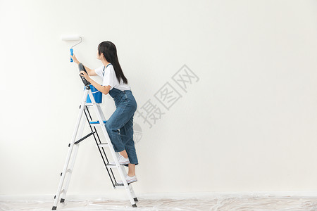 青年女性爬梯子刷墙图片