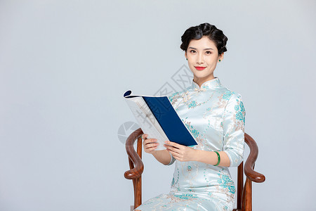 旗袍美女坐椅子上看书高清图片
