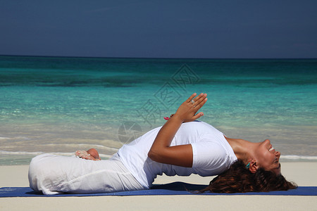 拱背在巴哈马拿骚天堂岛海滩上做瑜伽的年轻女子背景
