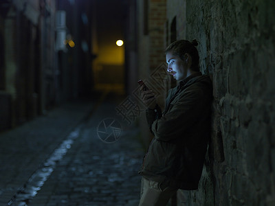 手机墙素材年轻人在街上晚上靠在墙上用智能手机背景