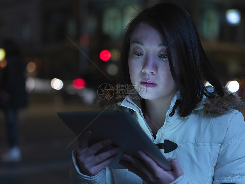 年轻女子晚上在街上，用数码平板电脑图片