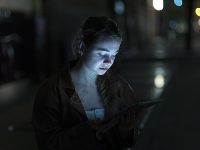 年轻女性使用数码平板电脑，户外，夜间，面部照明图片