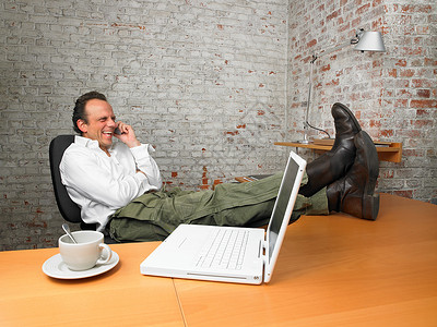双脚翘在办公桌上打电话的商务人士图片