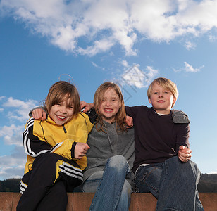 男性化3个孩子坐在矮墙上，微笑着背景