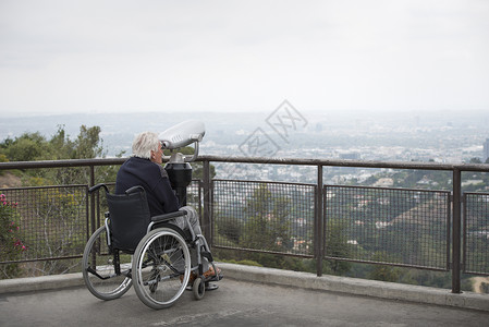 美国加利福尼亚州洛杉矶格里菲斯公园观景台投币双筒望远镜观看城市的轮椅老人图片