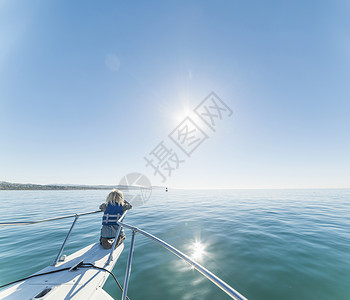 男孩跪在船上，帆船的船头朝远处看图片