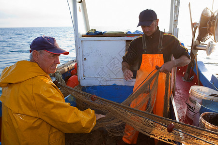渔民在船上卷起渔网高清图片