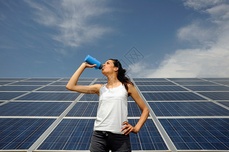 在太阳能板前喝水的女人图片