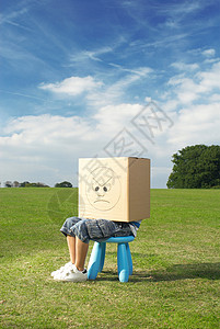 隐瞒小男孩坐在凳子上，头上戴着盒子背景