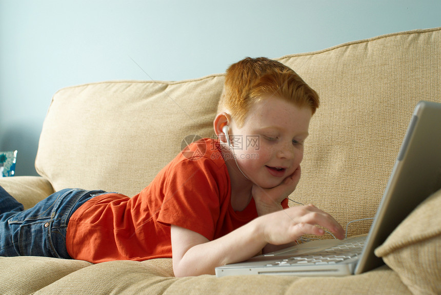 戴耳机的男孩在沙发上用笔记本电脑图片