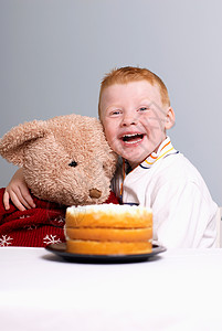 手拿泰迪熊玩具吃蛋糕的男孩图片