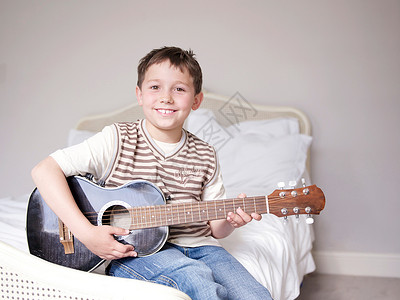 小男孩坐在床上弹吉他图片