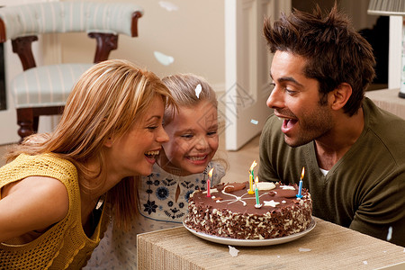 蛋糕女孩父母和孩子过生日吹灭蜡烛背景