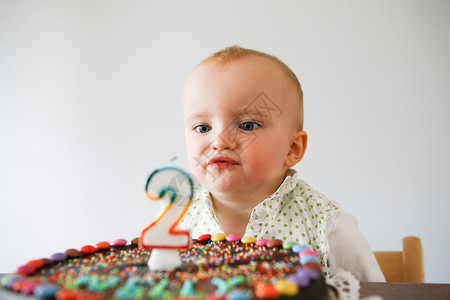 1岁生日蛋糕婴儿在生日蛋糕前吹蜡烛背景