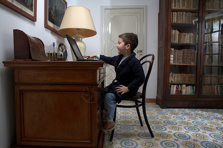 坐在桌旁用笔记本电脑的男孩图片