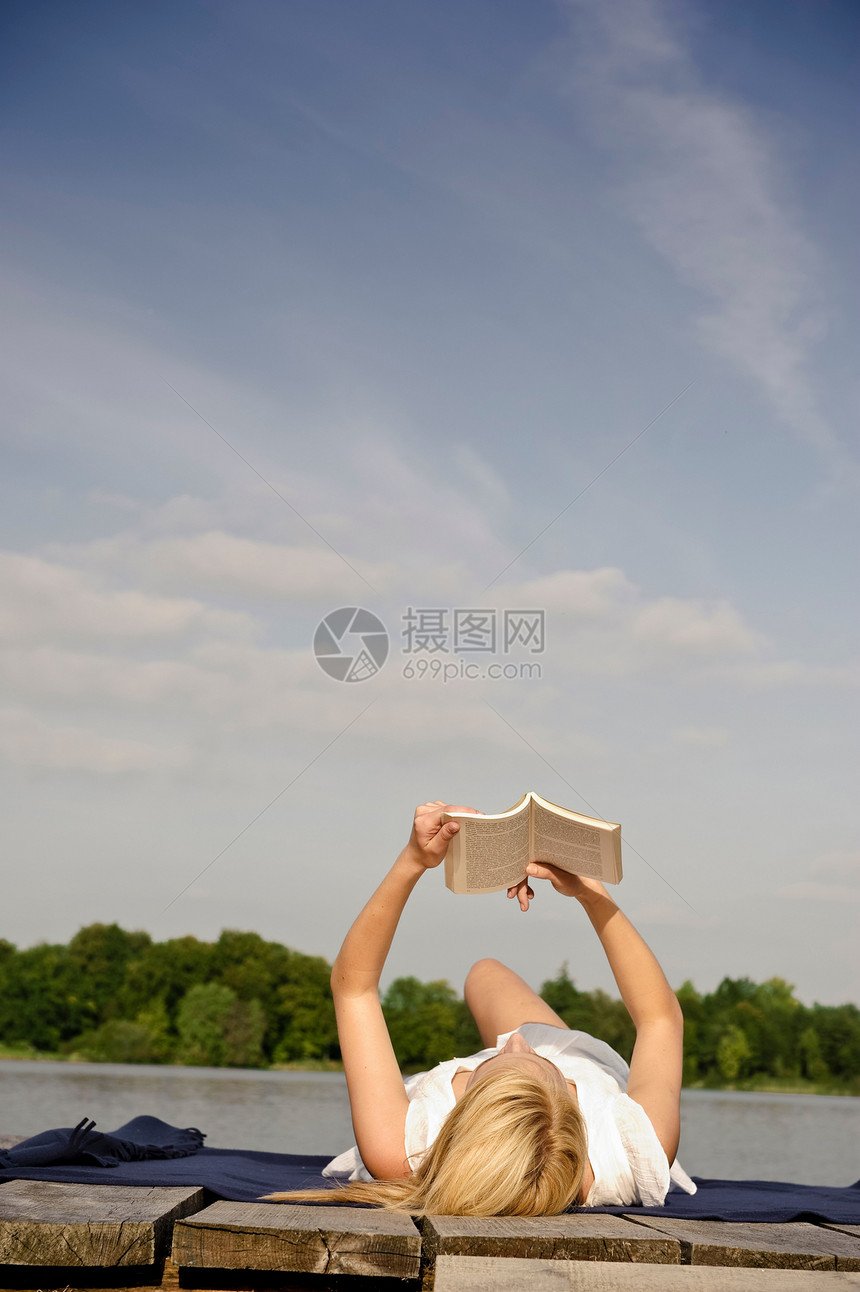 年轻女子躺在毯子上看书图片