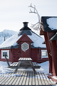 挪威斯瓦尔巴龙伊尔拜恩雪中的传统木屋和野餐长椅图片