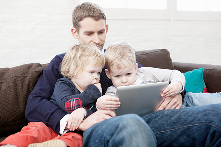 父亲在沙发上和儿子女儿一起使用数字平板电脑图片