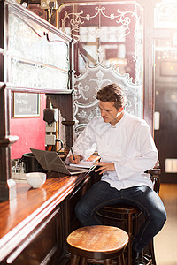 年轻的厨师坐在酒吧的凳子上用笔记本电脑图片