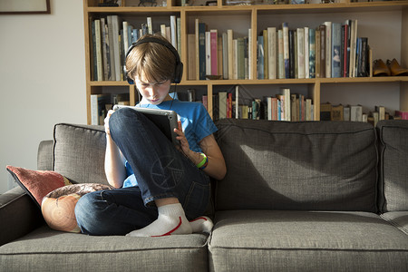 男孩在耳机上听音乐并使用数字平板电脑图片