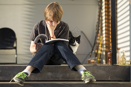 男孩坐在台阶上看书，猫从后面窥视图片