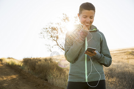 阳光山上成熟的女性跑步者选择智能手机音乐图片