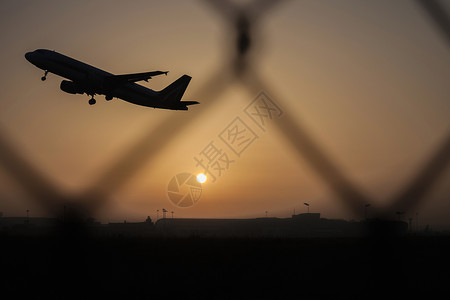 日落时分起飞的飞机，透过铁丝网看去图片