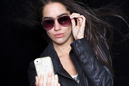 戴太阳镜的年轻女子的肖像，使用智能手机拍摄自画像图片