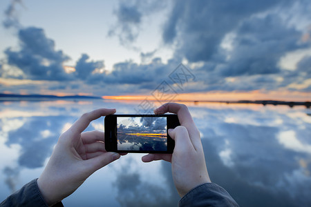 手机水拍摄日落时湖面倒影的人，英国西柯比背景